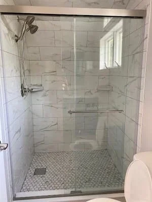 Walk-in shower with white subway tile walls, frameless glass door, and hexagonal mosaic floor tile
