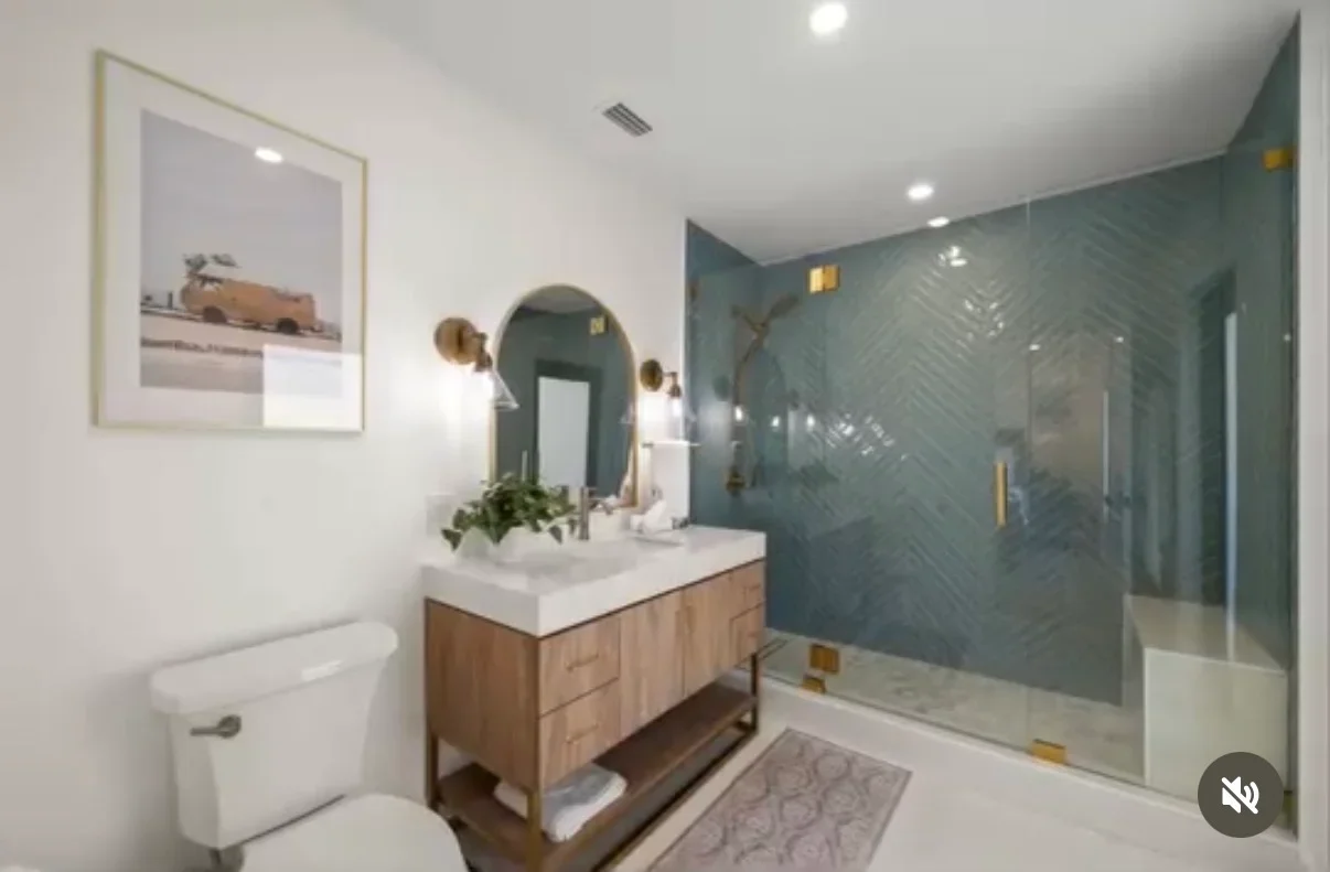 Modern bathroom with teal tile shower, white quartz counters, wood vanity, and brass fixtures