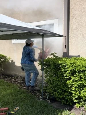 Motorized retractable awning with dark fabric installed over patio with hedges and lawn