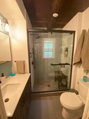 Renovated bathroom with frameless glass shower, white vanity, and dark ceiling
