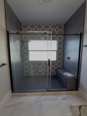 Frameless glass shower enclosure with geometric tile surround and polished concrete floor