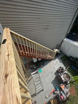 Newly constructed pressure-treated wood deck with white railings and balusters attached to house