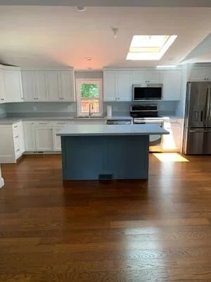 White kitchen cabinets, blue island, stainless appliances, hardwood floors, skylight