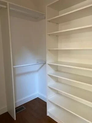 White walk-in pantry with adjustable shelving and dark flooring
