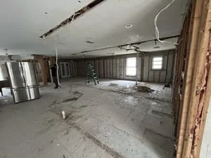 Empty kitchen space after demolition, showing concrete floor, exposed ceiling, and wooden door frame
