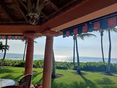 Wooden post-and-beam patio structure with striped awning overlooking ocean and landscaped grounds